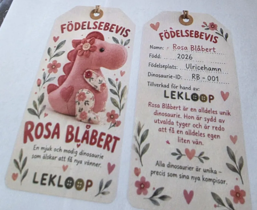Födelsebevis för Rosa Blåbert, en rosa dinosaurie med blomma. Född 2026 i Ulricehamn, dinosaurie-ID RB-001, tillverkad för hand av Lekloop