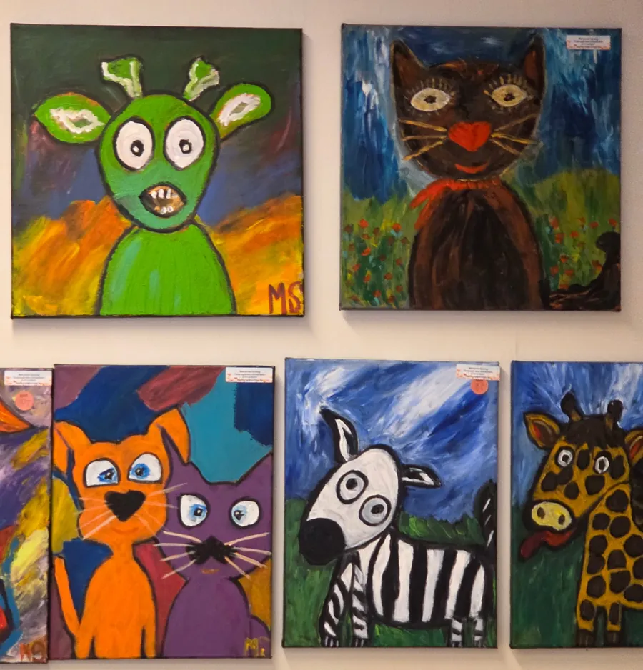 Tavlor med en grön figur, en svart katt med röd rosett, en orange och en lila katt, en zebra och en giraff