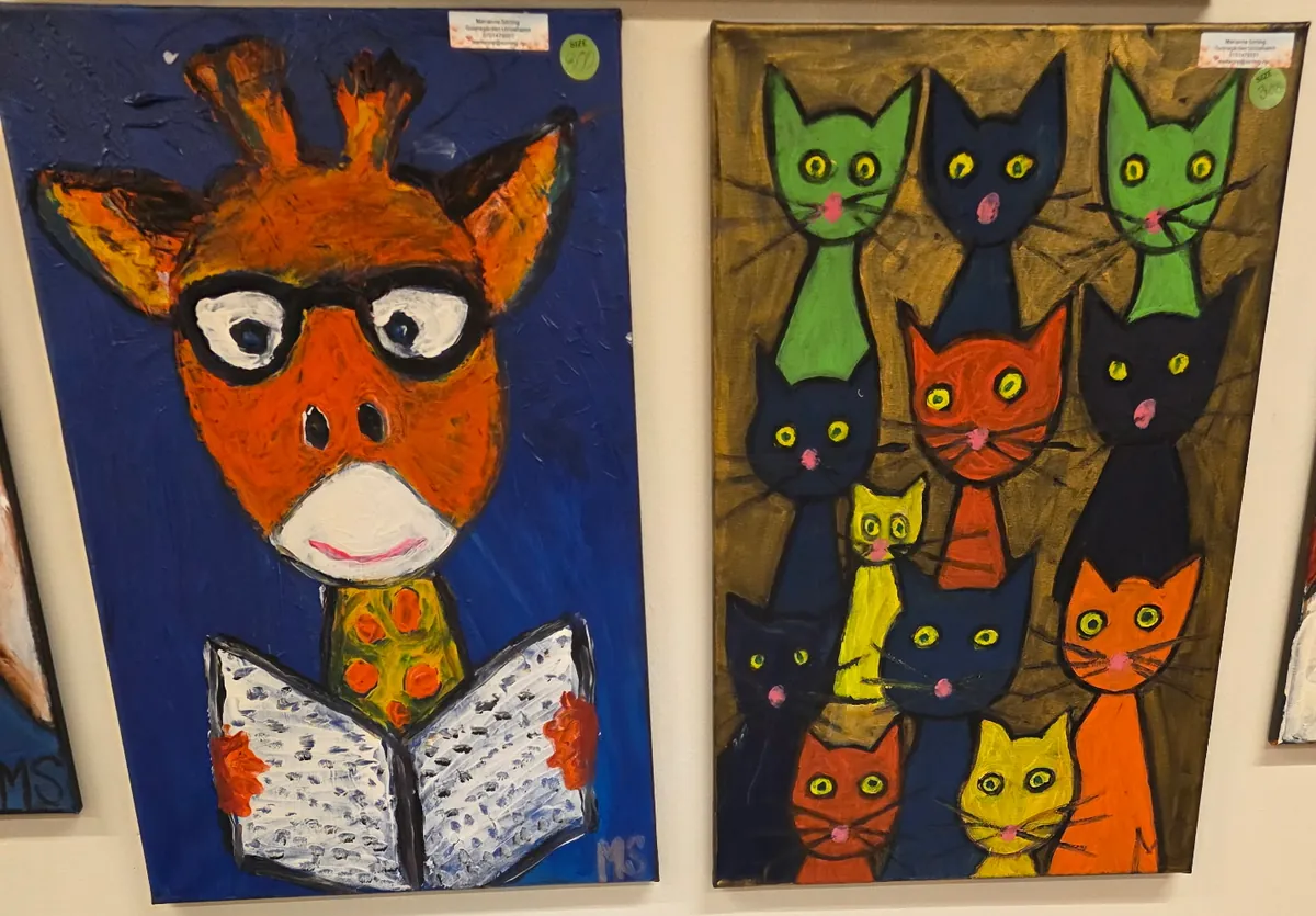 Tavla med en giraff med glasögon som läser en bok, bredvid en tavla med färgglada katter på guldbakgrund