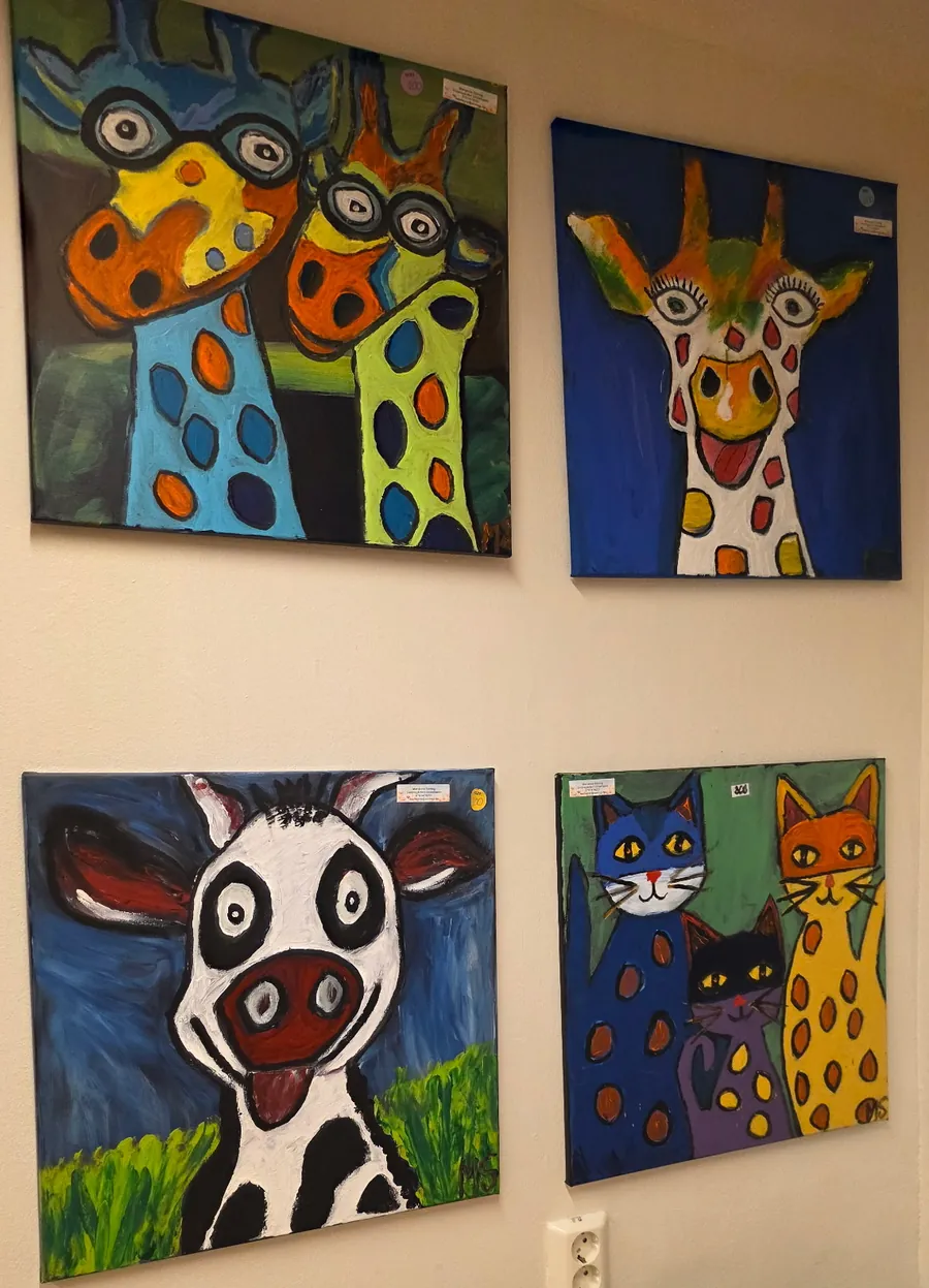 Fyra tavlor på väggen: två giraffer med glasögon, en skrattande giraff, en ko med utsträckt tunga och tre katter